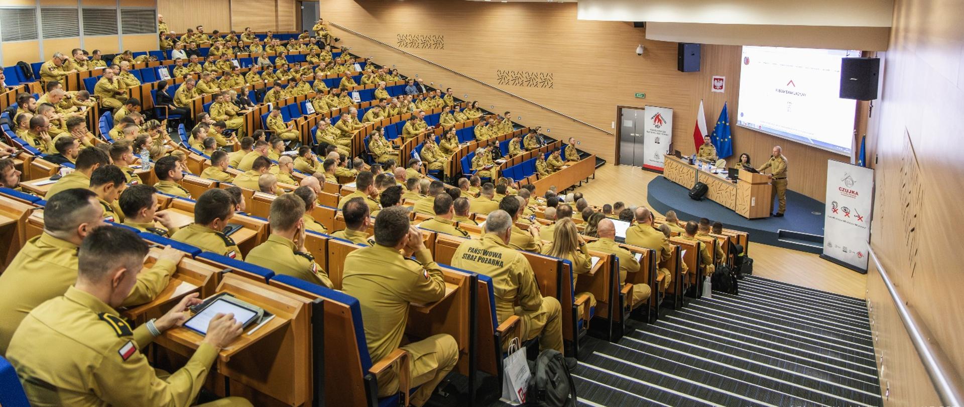 Widok ogólny dużej auli szkoleniowej Centralnej Szkoły PSP w Częstochowie wypełnionej funkcjonariuszami PSP uczestniczącymi w konferencji.