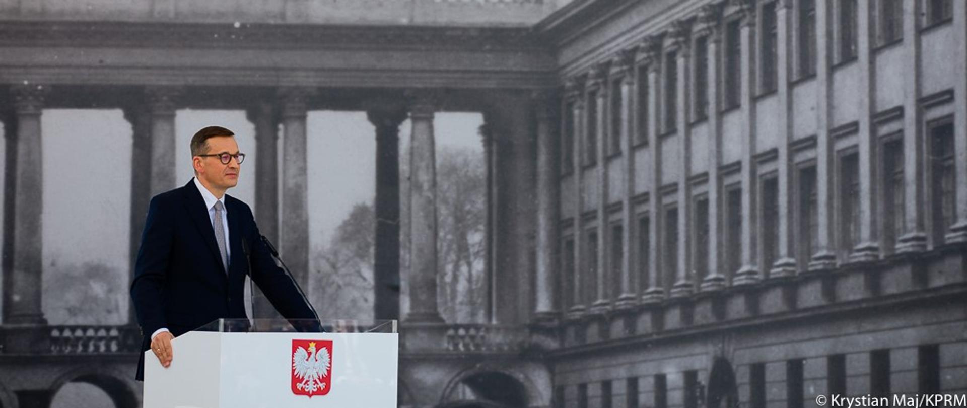 Premier Mateusz Morawiecki stoi przy mównicy podczas przemówienia.