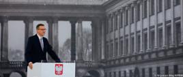 Premier Mateusz Morawiecki stoi przy mównicy podczas przemówienia.