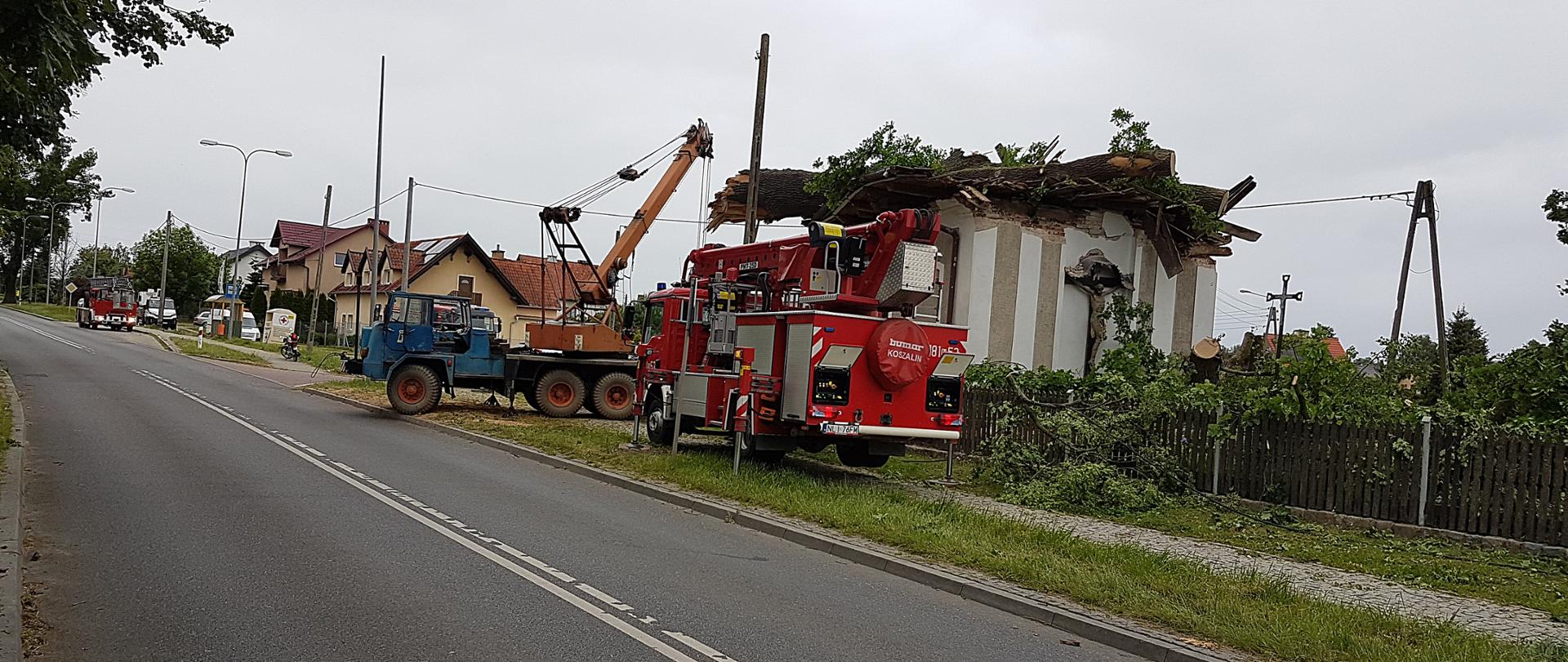 Zdjęcie przedstawia podnośnik lidzbarskiej straży oraz prywatny dźwig podczas akcji związanej ze ściągnięciem konaru drzewa znajdującego się na dachu obiektu sakralnego
