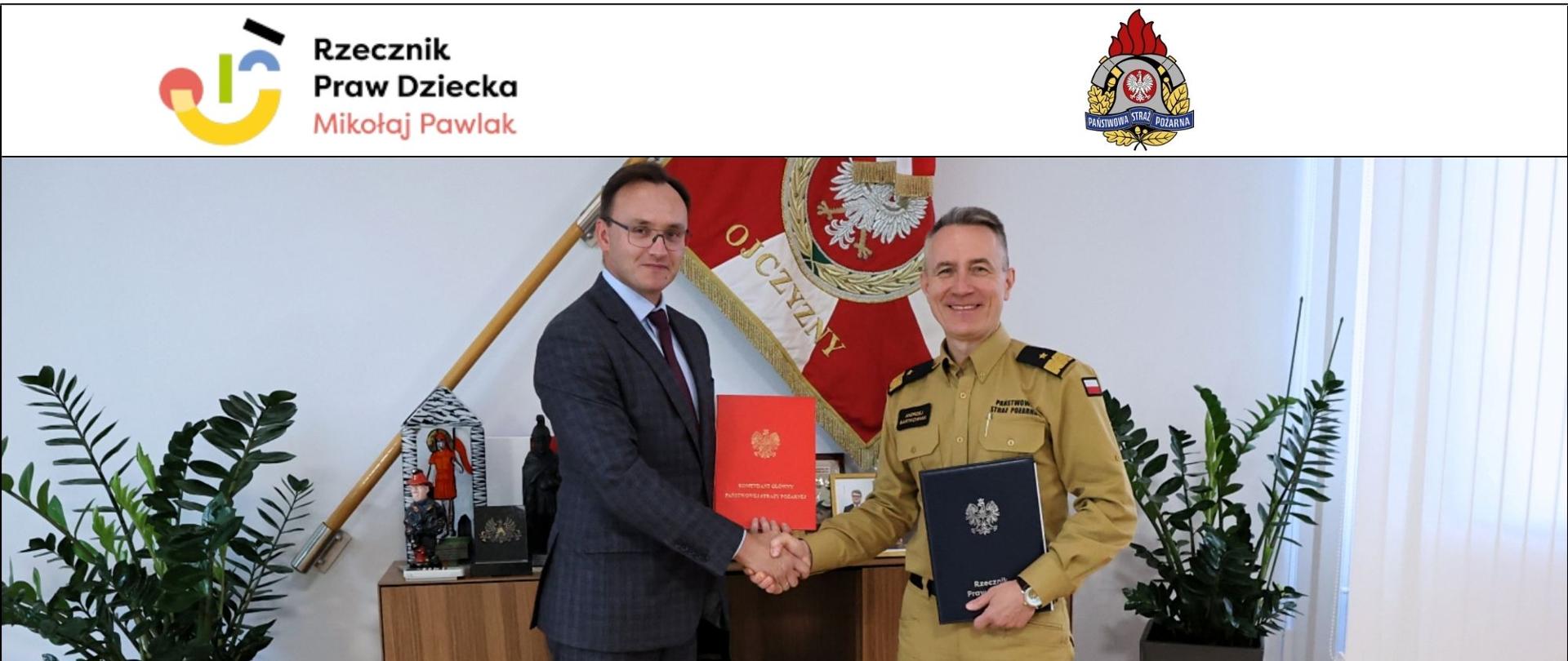 Komendant Główny (po prawo) i Rzecznik Praw Dziecka (po lewo) pozują do zdjęcia podając sobie dłonie i trzymając list intencyjny