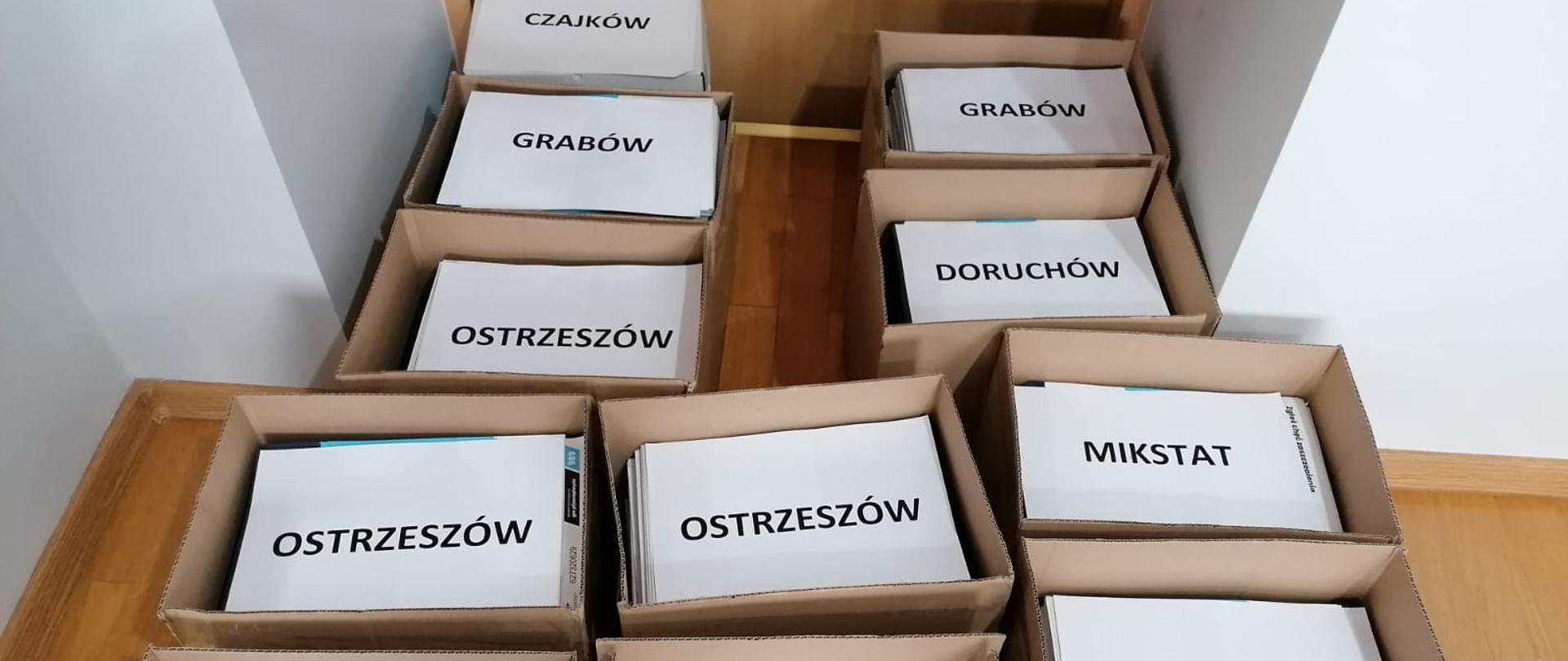 Na zdjęciu widoczne kartony w których znajdują się ulotki propagujące akcję szczepień. Zdjęcie wykonane w porze dziennej w pomieszczeniu biurowym.