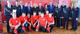 uczestnicy uroczystości wręczenia promes dla młodzieżowych drużyn pożarniczych pozują do zdjęcia zbiorowego wśród nich dzieci z młodzieżowej drużyny pożarniczej, strażacy druhowie, posłowie i senatorowie RP, przedstawiciele władz samorządowych