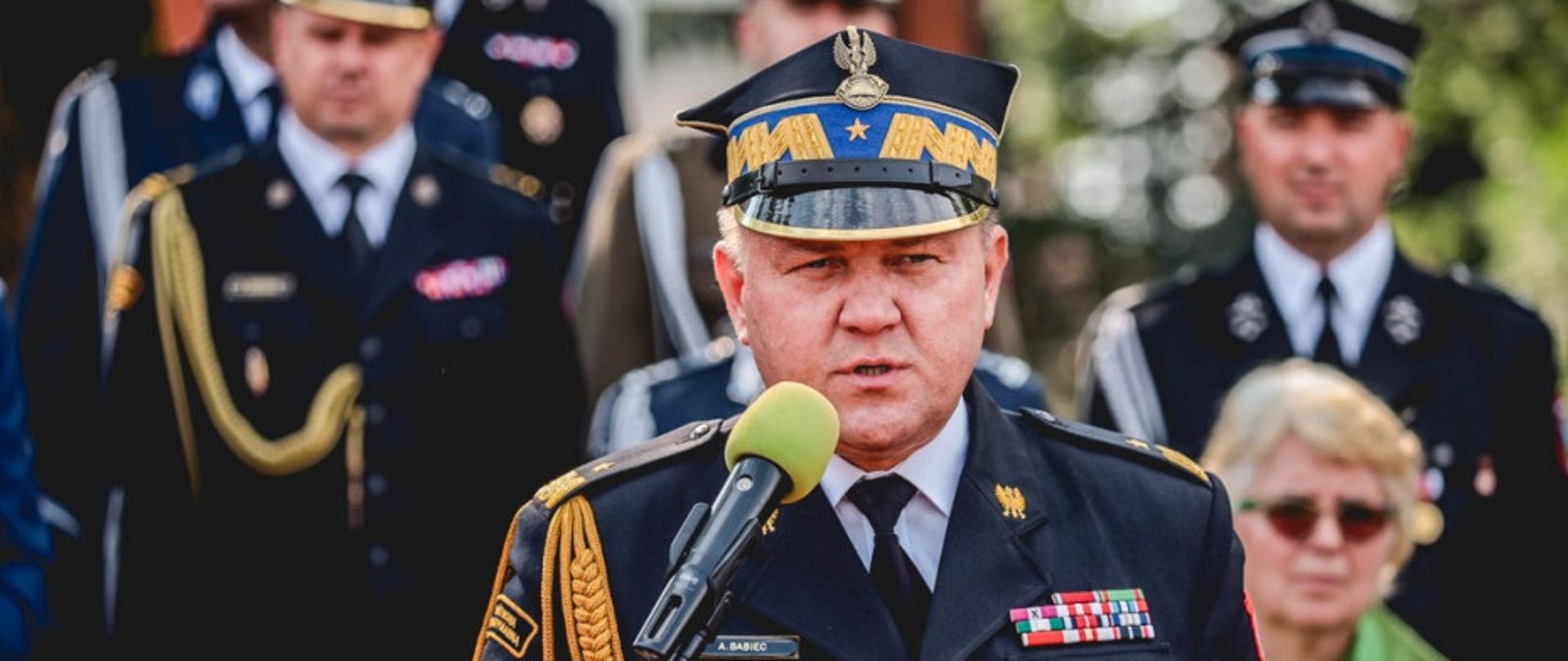 Fotografia wykonana podczas Jubileusz 155 lecia powstania jednostki OSP w Mielcu na stadionie miejskiego ośrodka sportu i rekreacji &quot;Gryf&quot;. Na zdjęciu stoją w jednym szeregu goście zaproszenie na uroczysty apel przed wyróżnieniem ich medalami za zasługi dla pożarnictwa. Za nimi widać strażaków druhów z pocztami sztandarowymi. Stojący na pierwszym planie funkcjonariusze ubrani w mundury PSP i Policji. Osoby cywilne ubrane w garnitury.