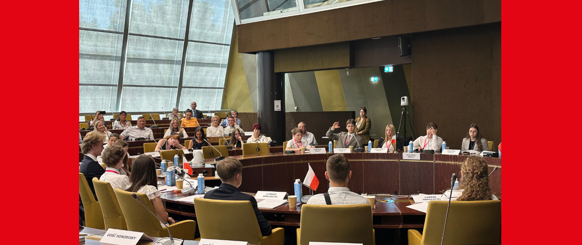 Sala plenarna i na niej młodzi deputowani, młoda osoba podnosi rękę