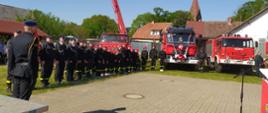 Zdjęcie przedstawia gości i pojazdy strażackie podczas uroczystego apelu