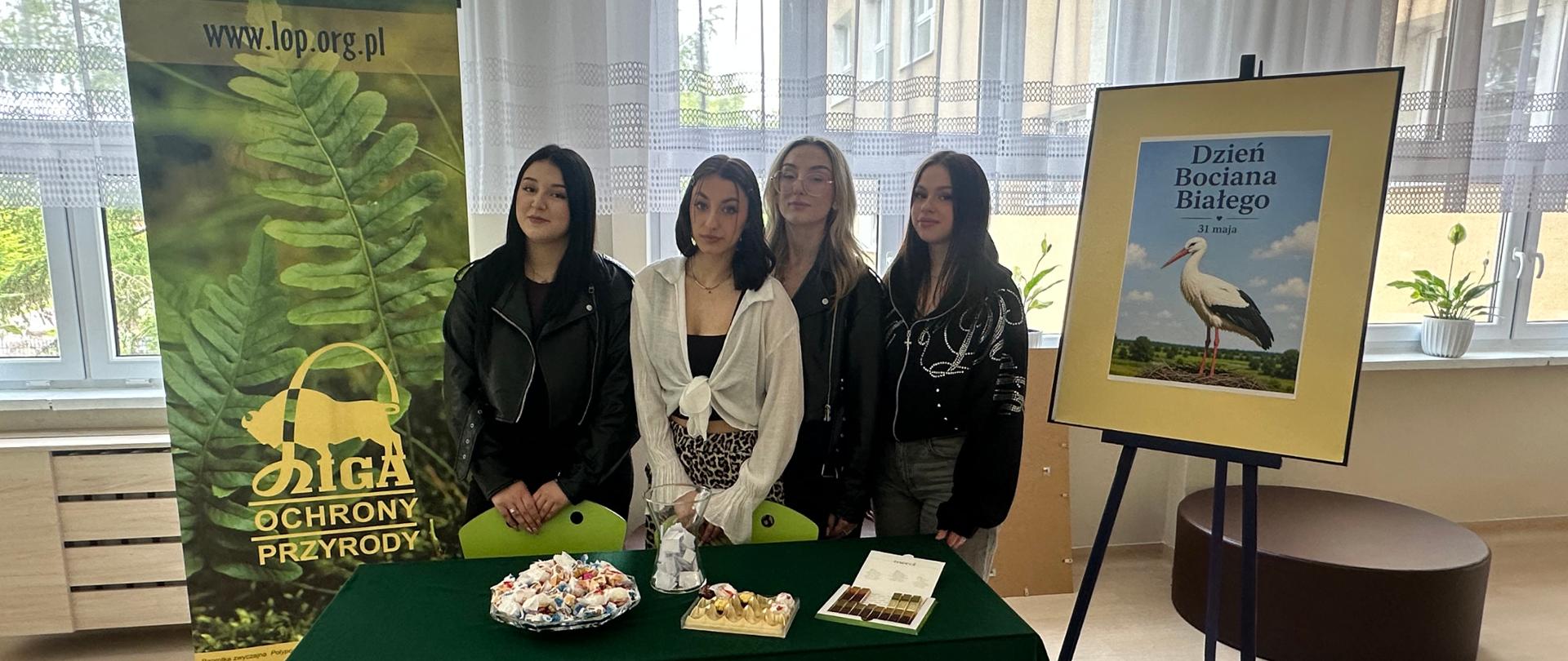 Uczestnicy stoją przy stole promocyjnym Ligi Ochrony Przyrody z materiałami edukacyjnymi i słodyczami
