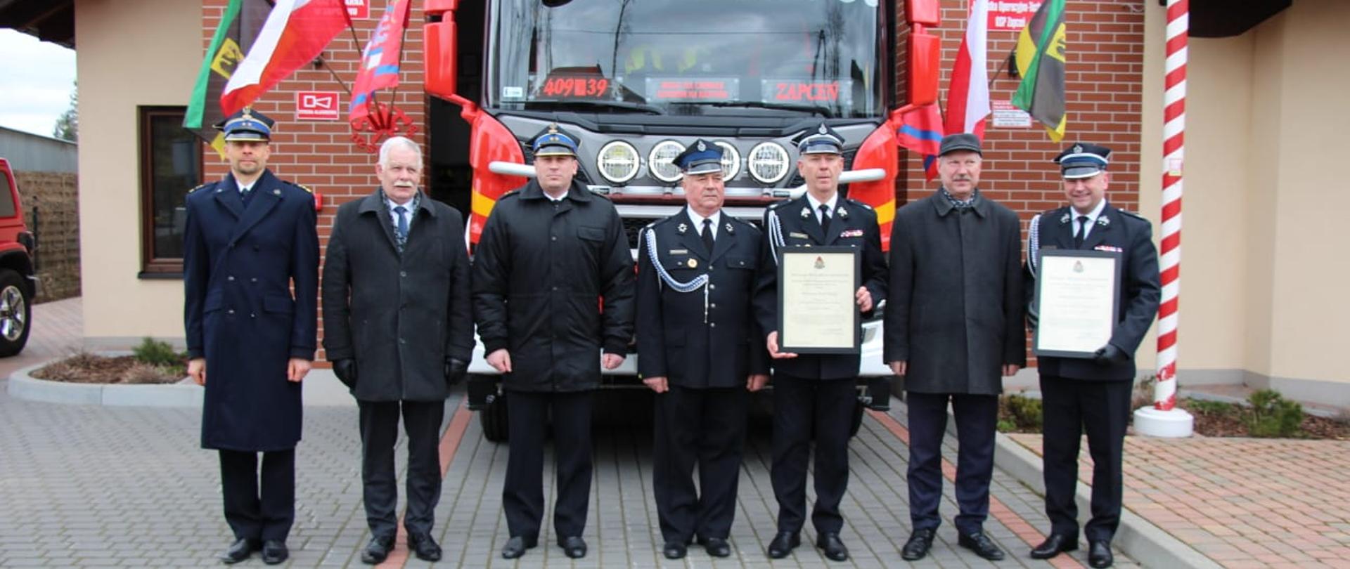Zdjecie przedstawia ustawionych przed samochodem strażackim strażaków umundurowanych w mundury galowe oraz Wicewojewodę Pomorskiego oraz Wójta Gminy Lipnica. Prezesi OSP w Zapceniu i Niedarzynie trzymają w rękach decyzje o włączeniu do KSRG