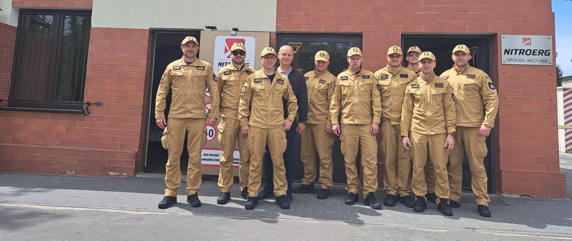 Wykładowcy Centralnej Szkoły PSP (9 funkcjonariuszy) w towarzystwie pracownika firmy NITROERG S.A. w Krupskim Młynie stojący na tle budynku firmowego