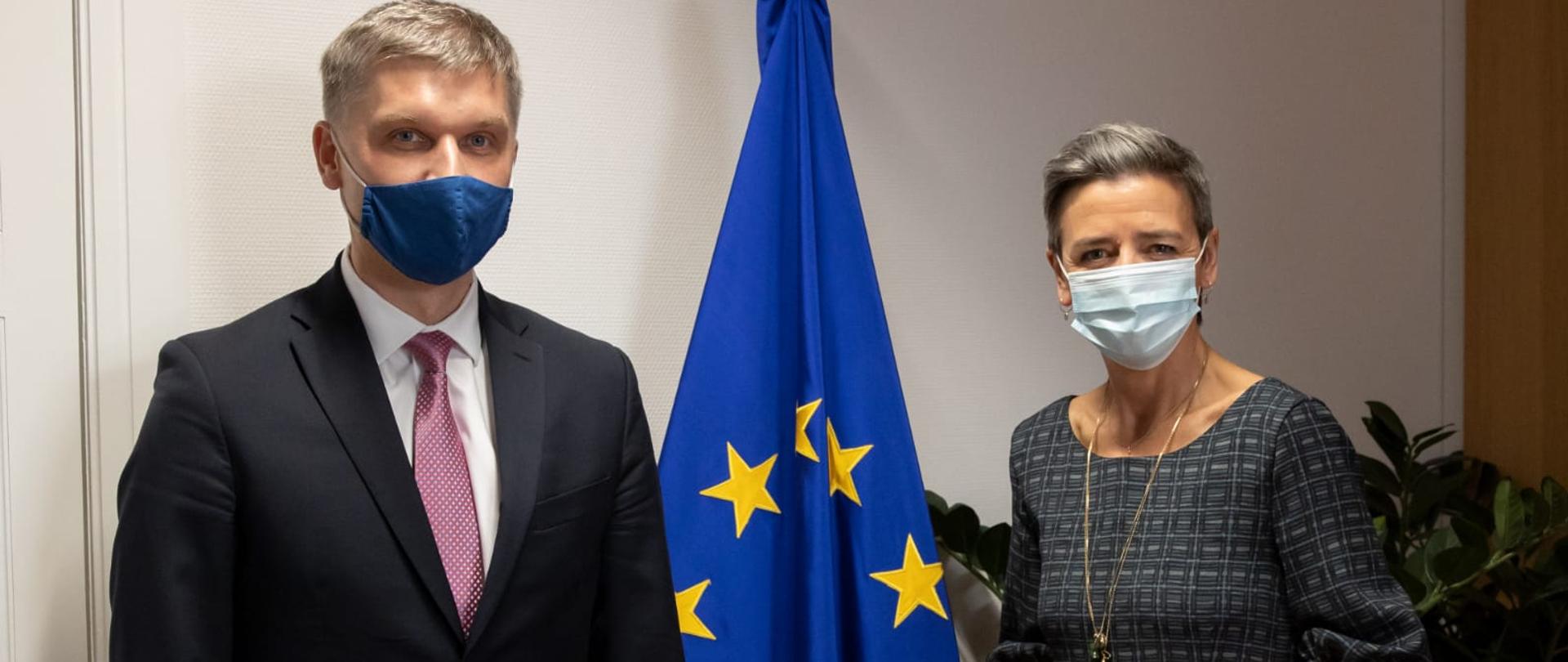 Minister rozwoju i technologii Piotr Nowak z wiceprzewodniczącą KE Margarete Vestager. Oboje w maseczkach, w tle flaga UE.