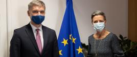 Minister rozwoju i technologii Piotr Nowak z wiceprzewodniczącą KE Margarete Vestager. Oboje w maseczkach, w tle flaga UE.
