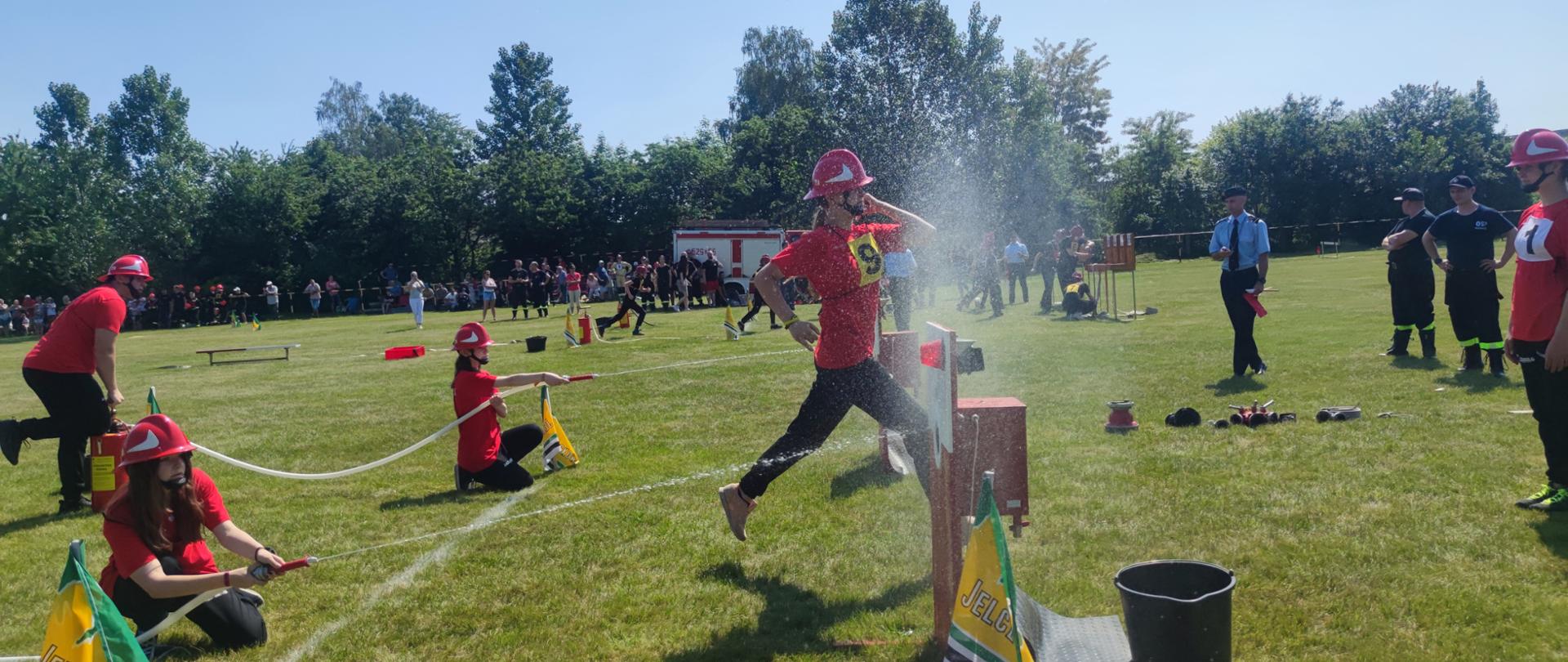 na zdjęciu widać młodych strażaków OSP podczas kolejnej konkurencji zawodów - przy użyciu hydronetek leją wodę do tarcz z nalewakami.