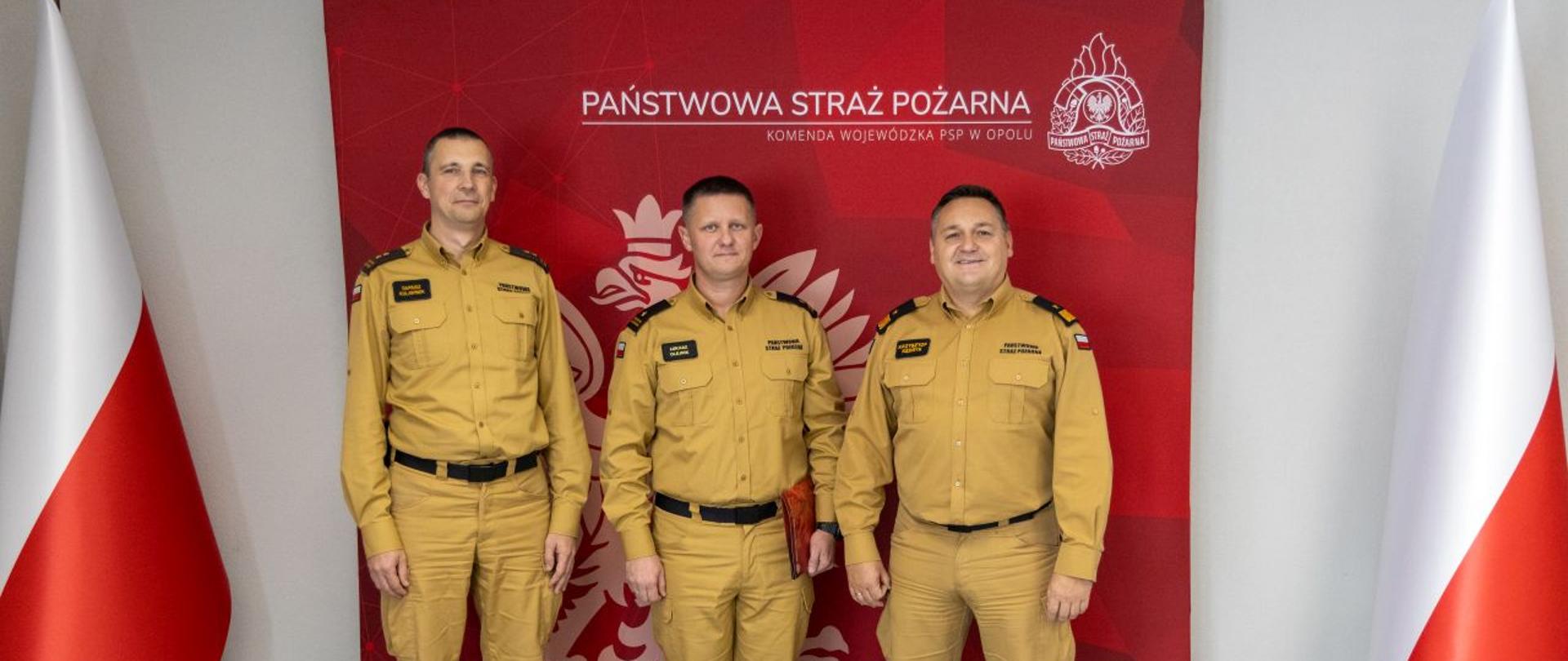 Wspólne zdjęcie nadbryg. Krzysztofa Kędryka Opolskiego Komendanta Wojewódzkiego PSP, bryg. Dariusza Kulawinka Komendanta Powiatowego PSP w Brzegu oraz mł. bryg. Łukasza Olejnika Zastępcy Komendanta Powiatowego PSP w Brzegu. W tle czerwony banner Państwowej Straży Pożarnej z napisem Komenda Wojewódzka PSP w Opolu koloru białego, białym logo PSP oraz białym Godłem Rzeczpospolitej Polskiej. Obok banneru stoją dwie Flagi RP po lewej i prawej stronie.