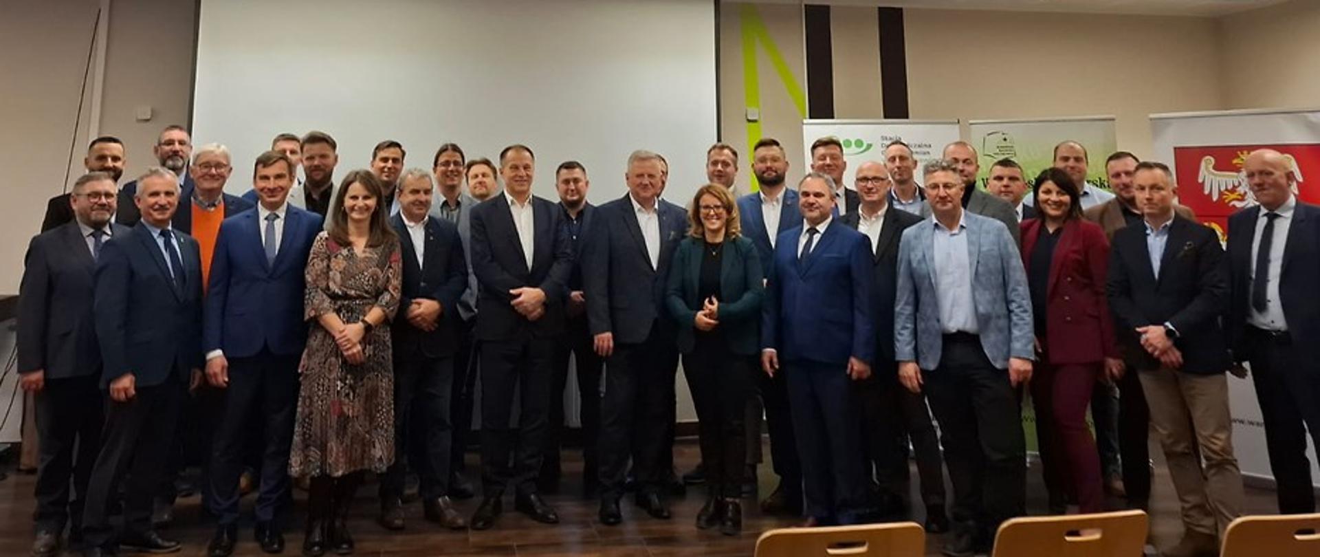 Grupa osób pozuje do wspólnego zdjęcia w sali konferencyjnej