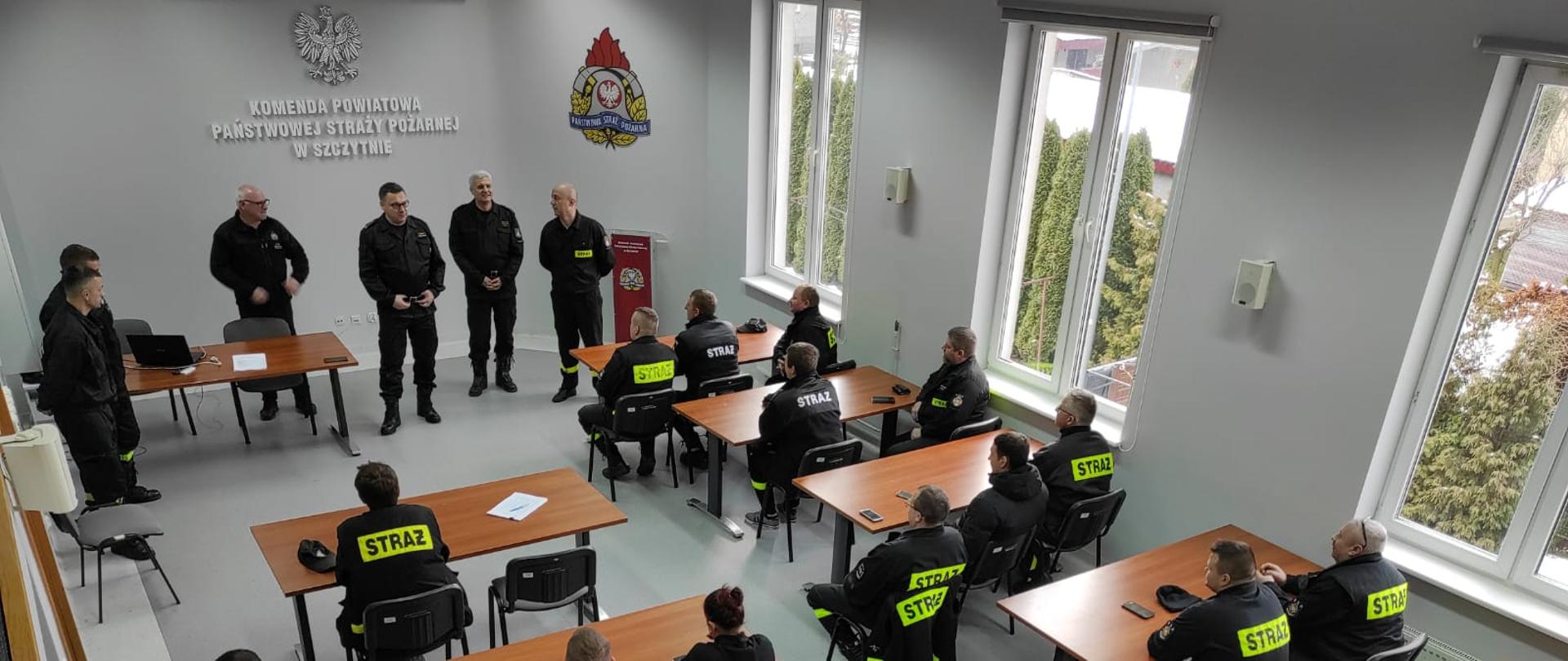 Zdjęcie przedstawia kadrę komendy powiatowej oraz przybyłego Zastępcę Warmińsko-Mazurskiego Komendanta Wojewódzkiego PSP st.bryg. Tomaszowi Ostrowskiemu podczas rozpoczęcia recertyfikacji kwalifikowanej pierwszej pomocy