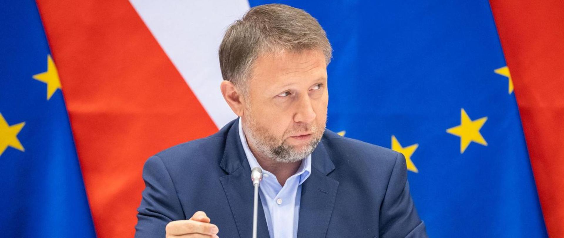 Minister Kierwiński mówi do mikrofonu. W tle flagi polski i unijne 
