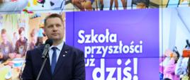 Minister Czarnek stoi i mówi do mikrofonu, za nim wielki ekran z napisem Szkoła przyszłości już dziś.
