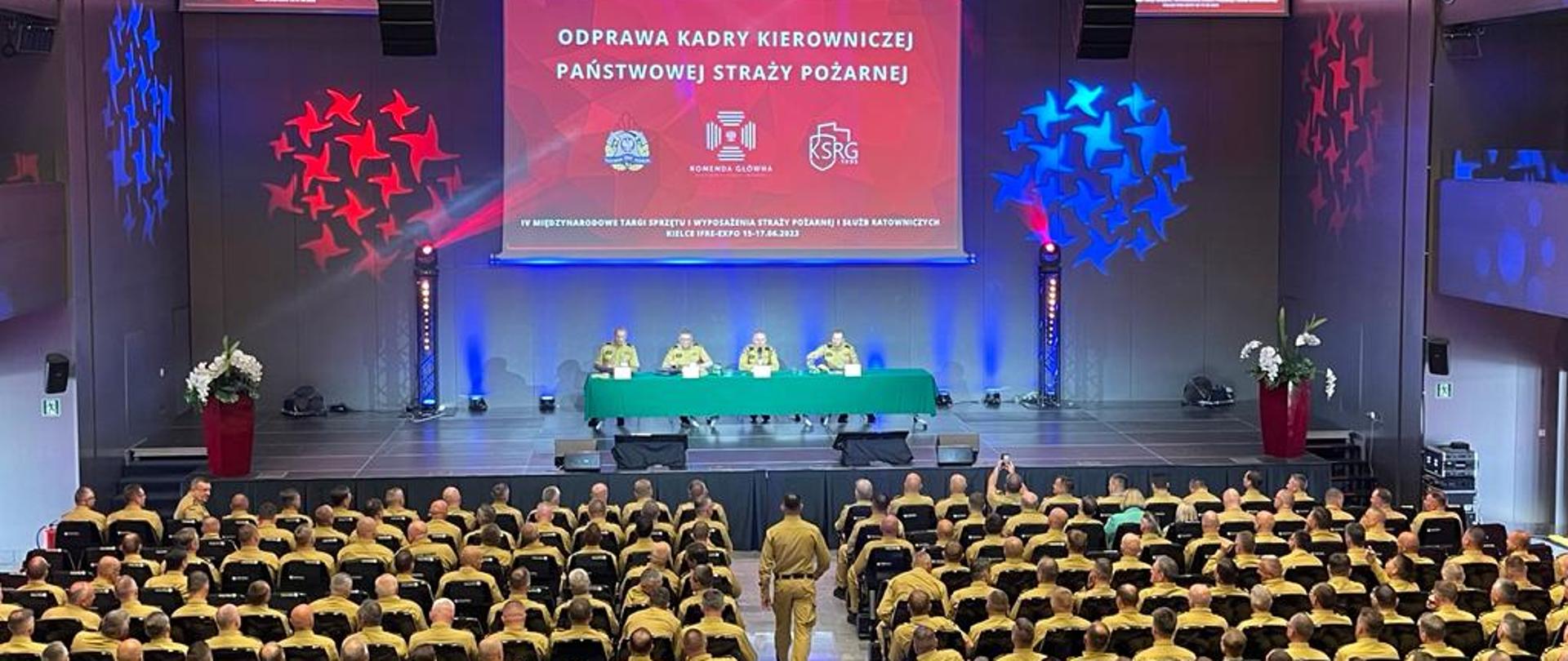 w dużej sali na krzesłach siedzą strażacy, na ekranie widać na czerwonym tle slajd z napisem odprawa kadry kierowniczej państwowej straży pożarnej
