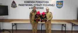 Kolorowa fotografia przedstawia wykonana w pomieszczeniu w pochmurny dzień. Przedstawia dwóch strażaków trzymających maskotki tzw. Żarki przekazane na licytację dla WOŚP. W tle napis Komenda Powiatowa PSP w Brzozowie.