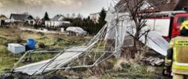 Na zdjęciu widzimy strażaka podczas usuwania skutków silnego wiatru. W tle widać samochód strażacki.