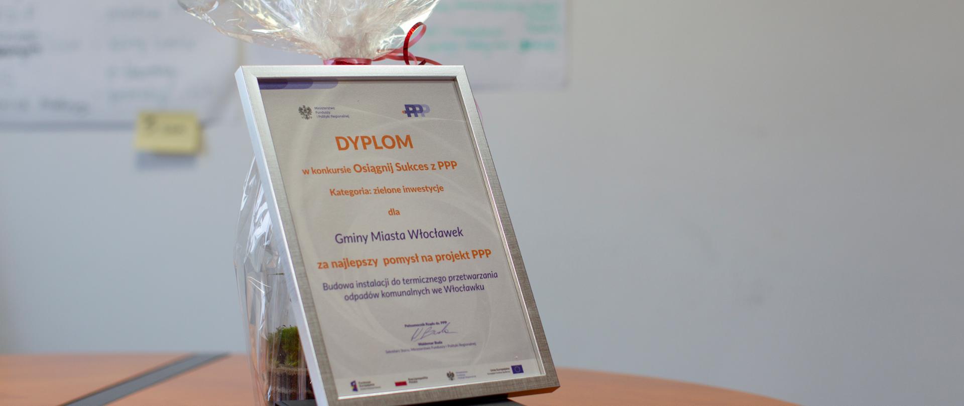 Na stole stoi dyplom w konkursie na najlepsze projekty realizowane w formule partnerstwa publiczno-prywatnego