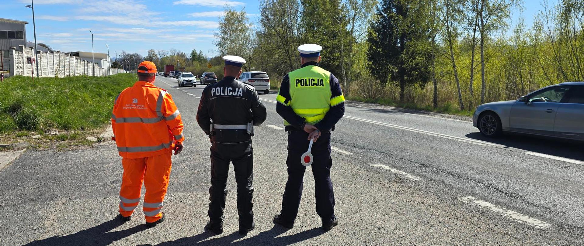 Policjanci i drogowiec czekają na zatrzymanie samochodu