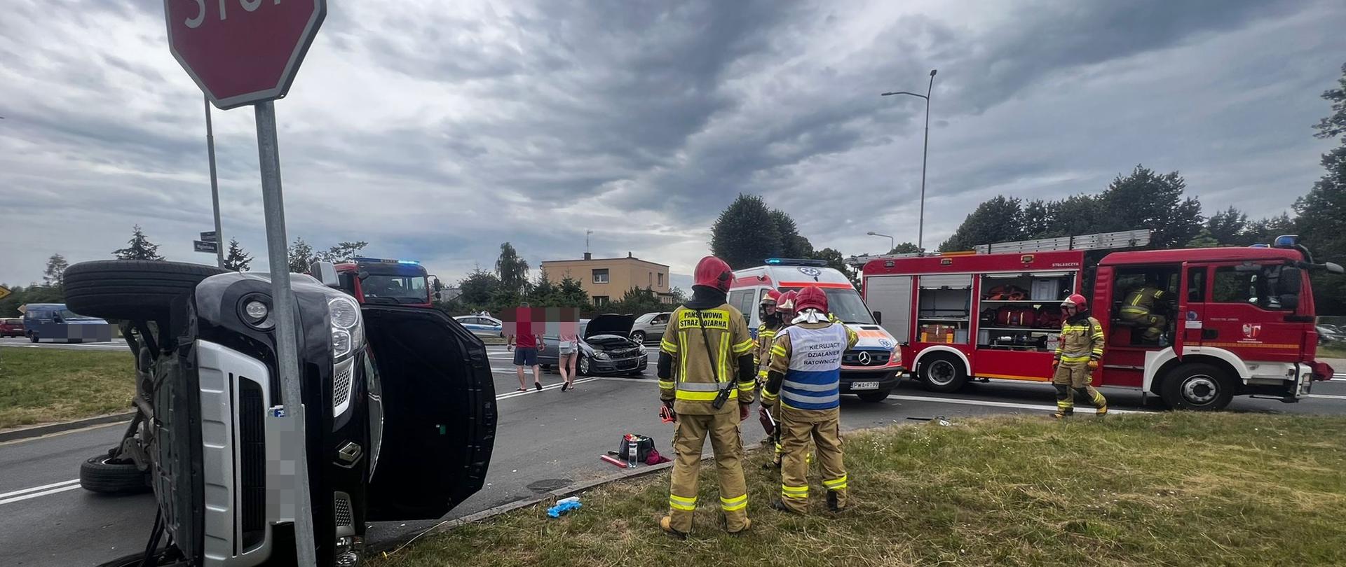 Na zdjęciu widać przewrócone auto na boku oraz służby ratownicze 