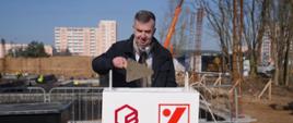 Na dworze nad betonowym pudłem z napisem Politechnika Bydgoska stoi minister Wieczorek i trzyma w ręku kielnię.