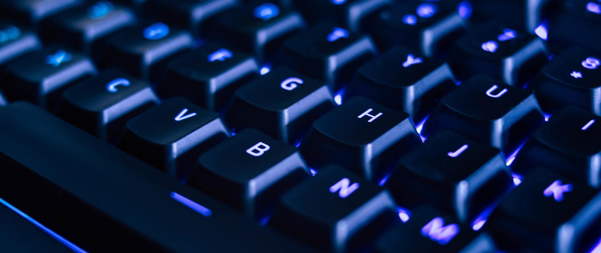 Częściowy widok klawiatury komputerowej podświetlonej na niebiesko. 