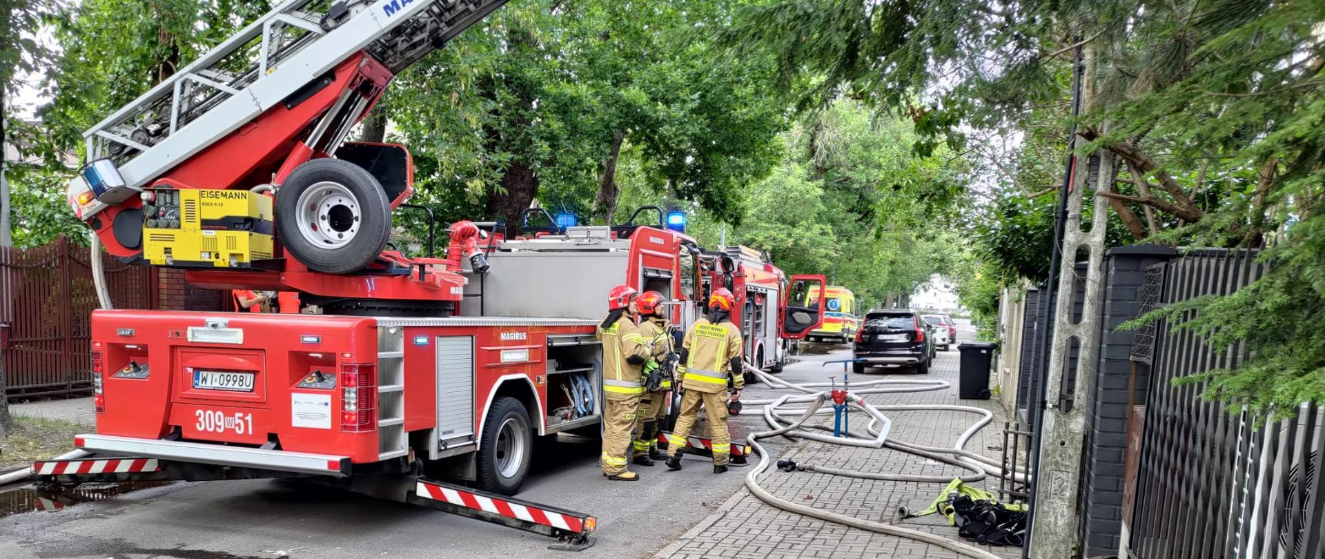 Na zdjęciu widoczne są samochody straży pożarnej, pracujący strażacy. Na zdjęciu widoczne są również linie wężowe oraz widoczna jest karetka pogotowia