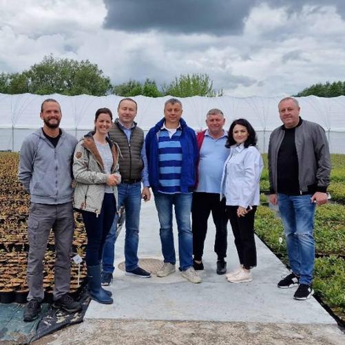 Grupa 7-osobowa pozuje do zdjęcia na plantacji, w tle duży rolniczy tunel foliowy.