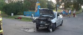 Samochód osobowy stoi na środku skrzyżowania. Ma uszkodzony cały przód po zderzeniu.