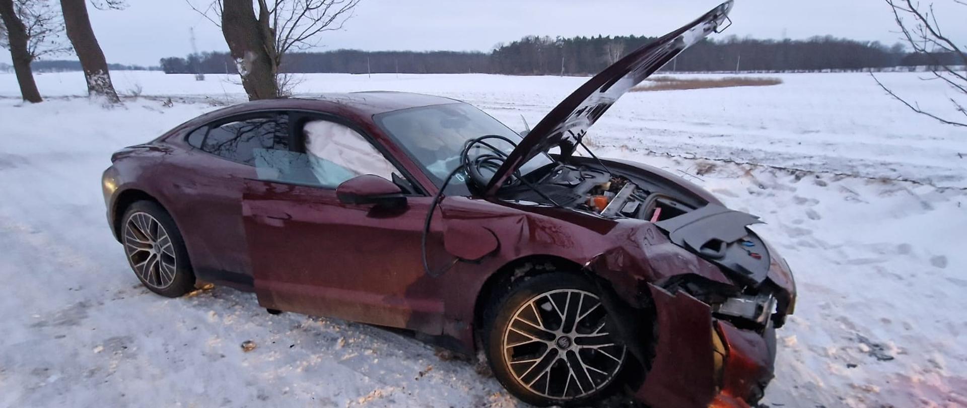 Bordowy samochód na drodze, ma uszkodzony prawy bok i przód, w koło śnieg