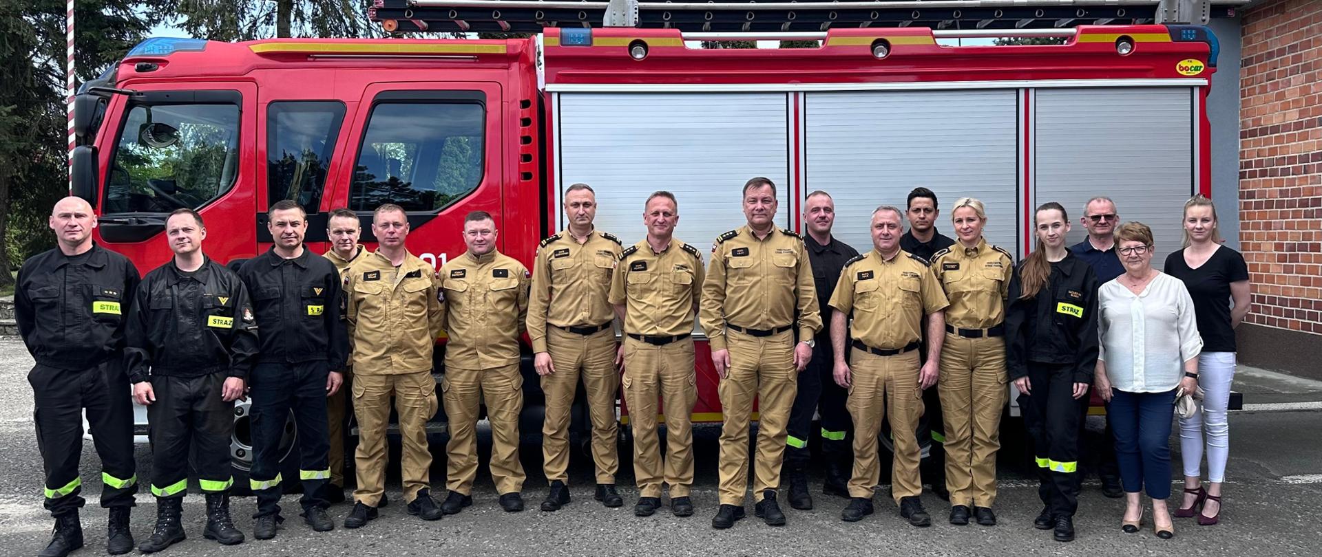 Na zdjęciu znajdują się strażacy w umundurowaniu służbowym i pracownicy cywilni ustawieni do zdjęcia na tle samochodu strażackiego 