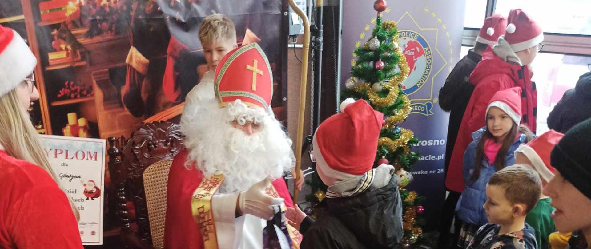 Na zdjęciu widoczny jest Mikołaj rozdający prezenty dzieciom podczas Spotkania z Mikołajem w KM PSP Krosno.