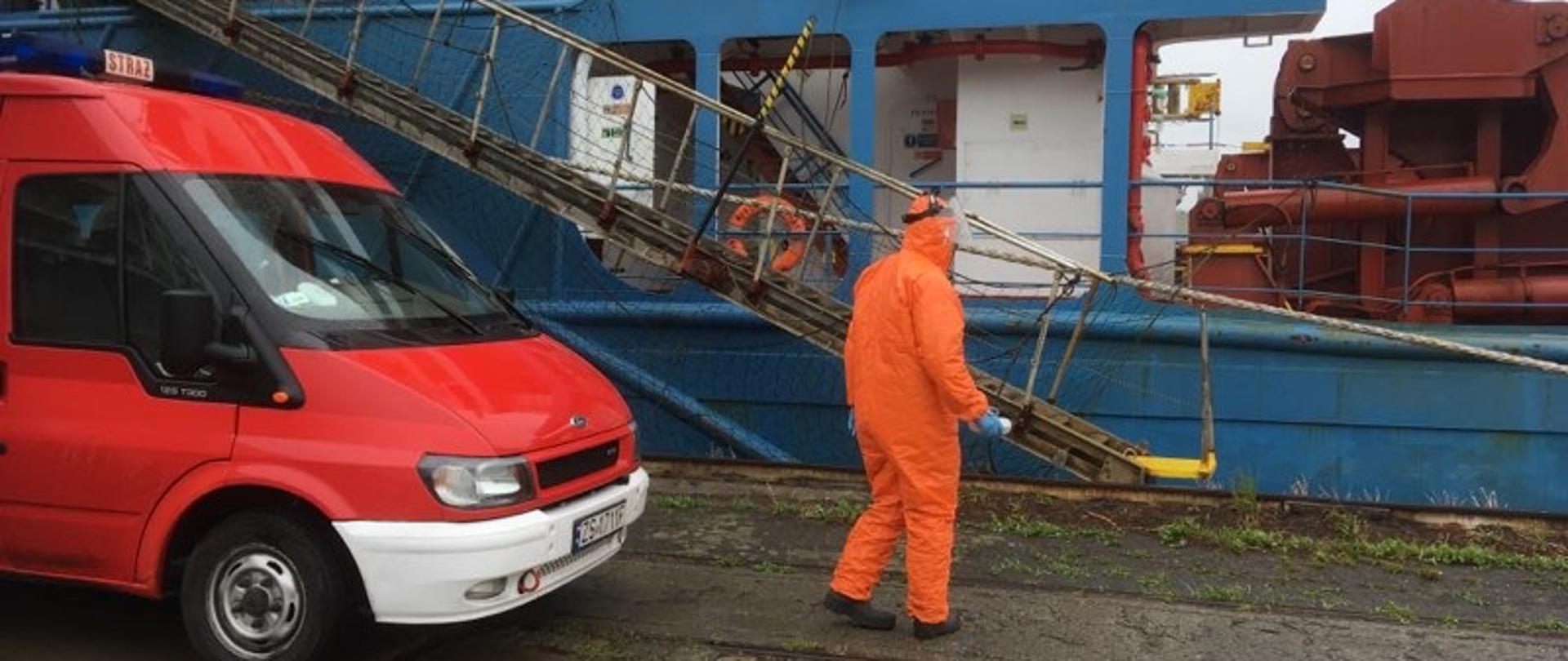 Strażak w ubraniu chemoodpornym wchodzący na statek w celu dokonania pomiaru temperatury członkom załogi statku