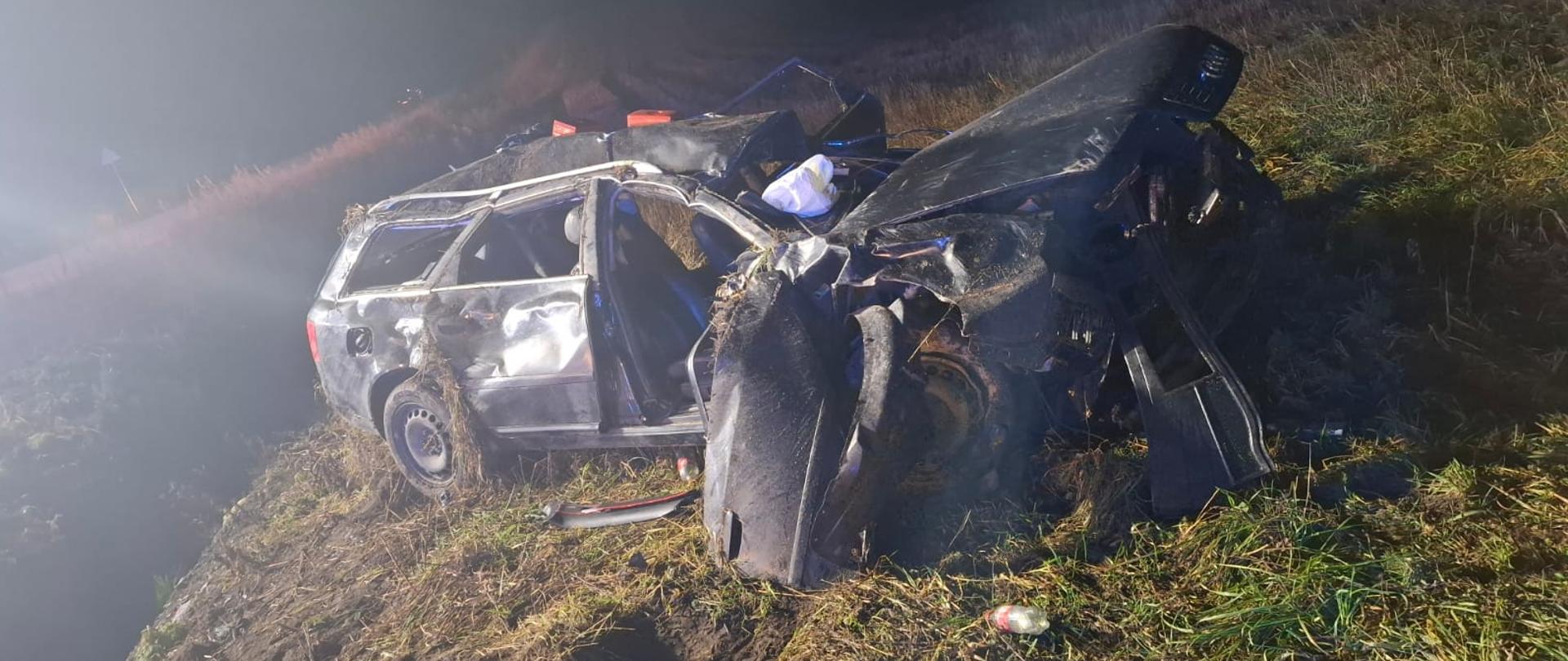 Na zdjęciu widoczny jest zniszczony pojazd osobowy, który podczas zdarzenia wypadł z drogi. Pojazd jest w całości zniszczony poprzez swoje uszkodzenia i liczne wgniecenia.