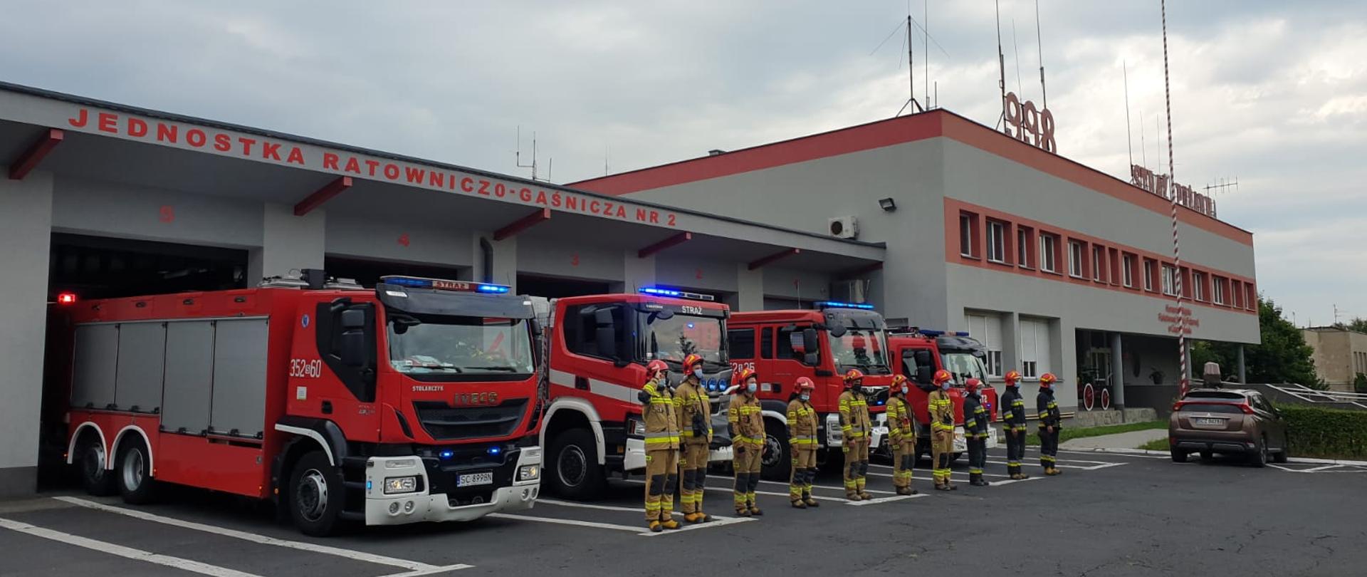 Zdjęcie przedstawia Funkcjonariusza Państwowej Straży Pożarnej oraz samochodach ratowniczo-gaśnicze ustawione przed budynkiem Jednostki Ratowniczo-Gaśniczej numer 2 w Częstochowie. Stażacy oddają hołd powstańcom w 77 rocznicy wybuchu Powstania Warszawskiego.