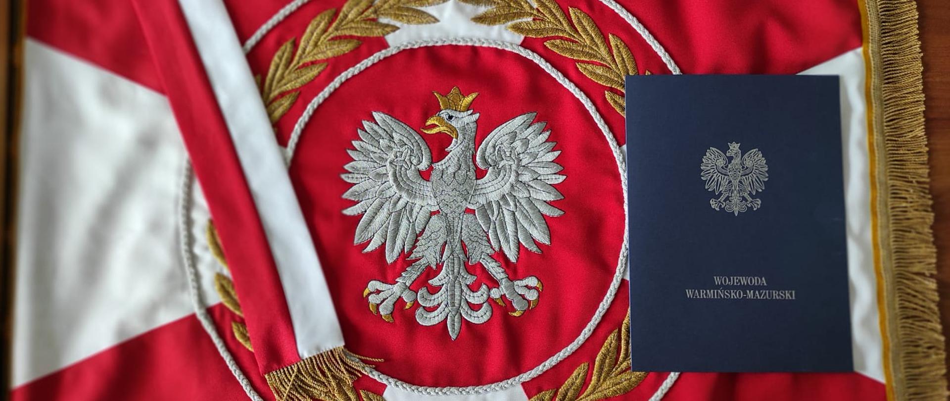 Zdjęcie przedstawia sztandar KP PSP w Szczytnie na którym leży teczka z dofinansowaniem na zakup samochodu ratowniczo-gaśniczego dla OSP Lipowiec