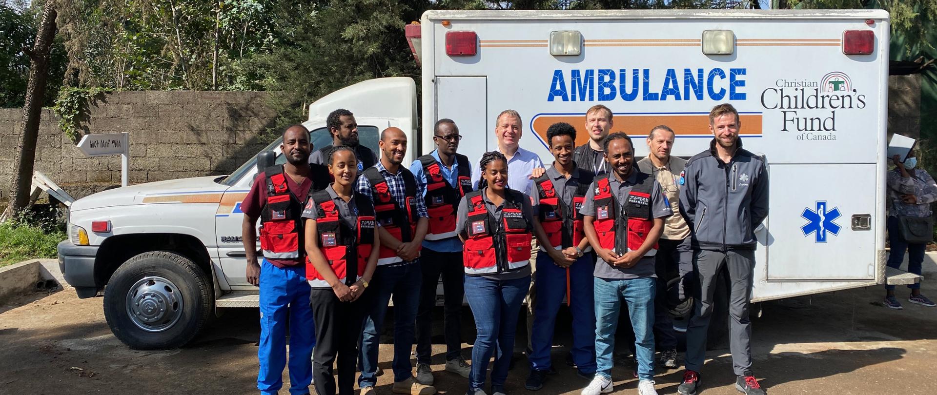 Ratownicy medyczni pozujący do zdjęcia na tle ambulansu.