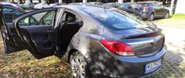 Samochód w kolorze czarnym - Opel Insignia, stoi przed budynkiem i ma otwarte drzwi.