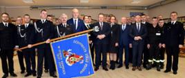 Strażacy stoją w grupie. Jeden z nich trzyma sztandar