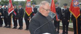 Jubileusz 95-lecia OSP Konary. Plac przed remizą strażacką. Ksiądz proboszcz odmawia modlitwę przed poświęceniem pamiątkowej tablicy. W tle poczty sztandarowe.