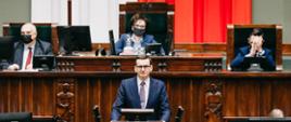 Premier Mateusz Morawiecki przemawia na mównicy sejmowej, w tle siedzi marszałek Elżbieta Witek.