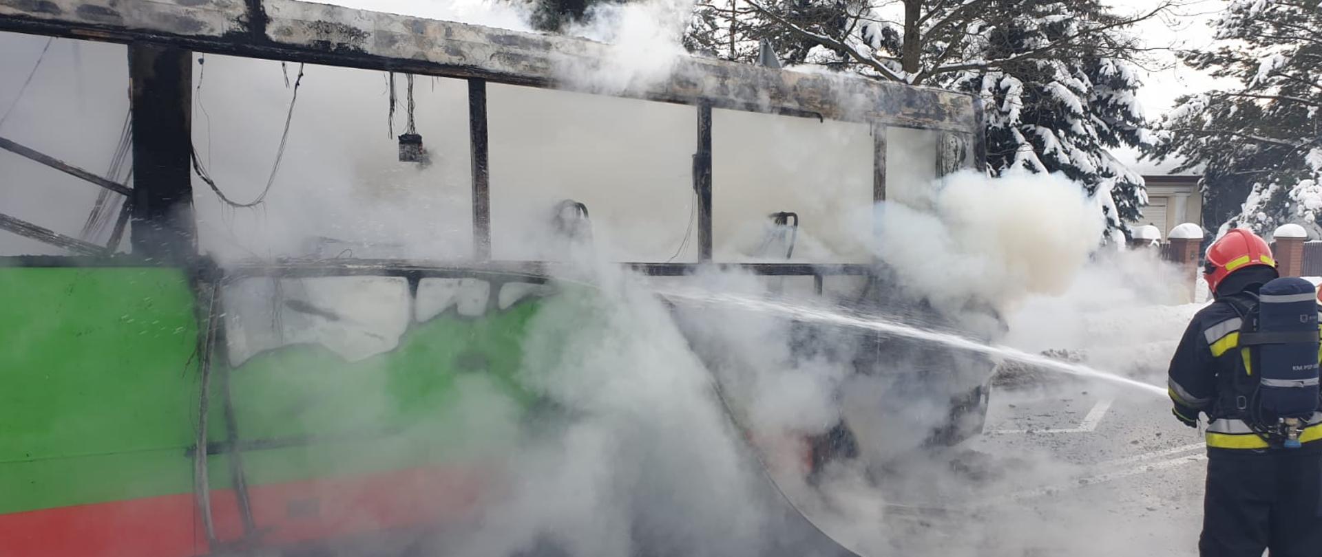 W tle pożar autobusu przy ul. 3-go maja w Mysłowicach i strażacy gaszący pożar.