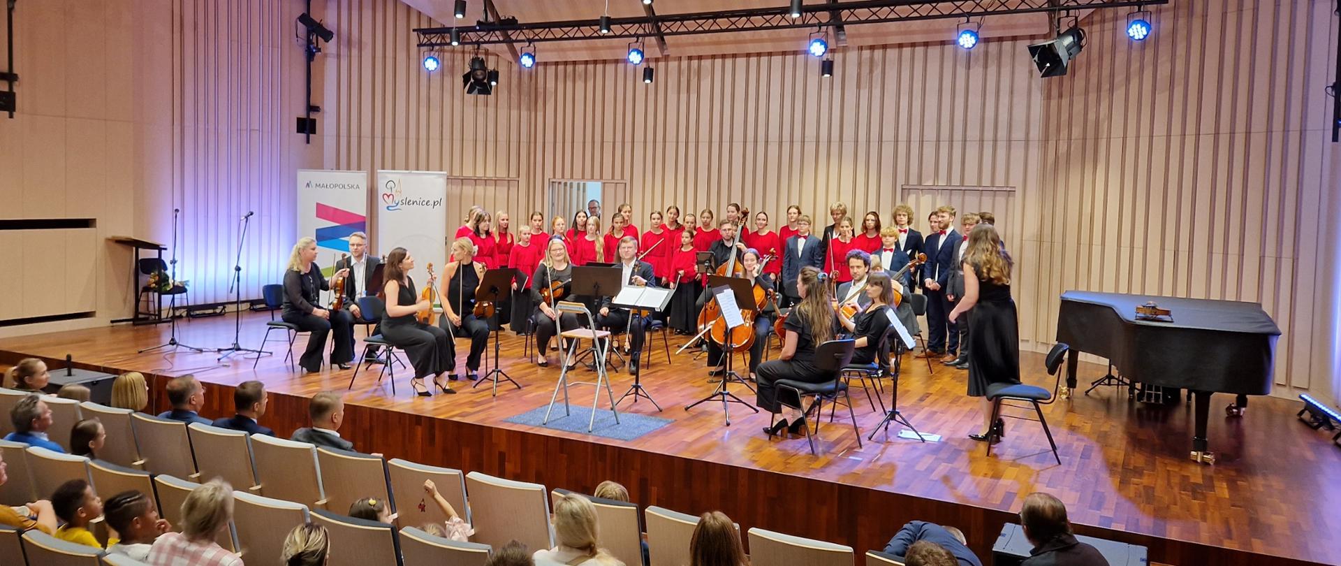 Chór i orkiestra na scenie w sali koncertowej.