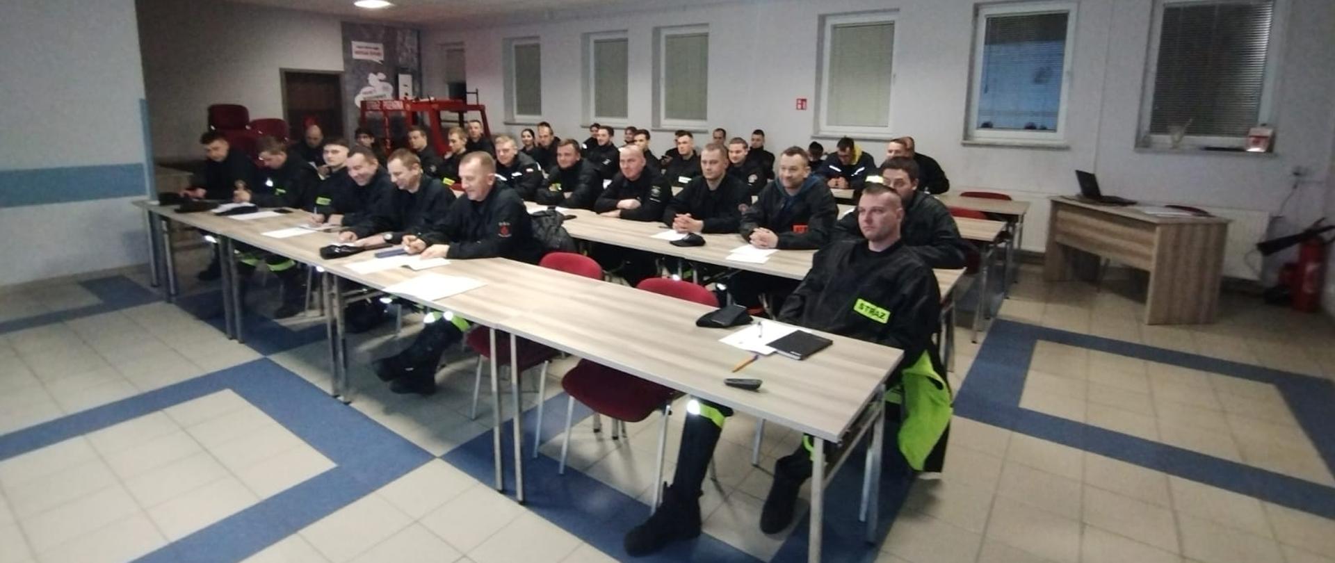 Uczestnicy kursu podstawowego OSP siedzący w czterech rzędach ławek na sali szkoleń.