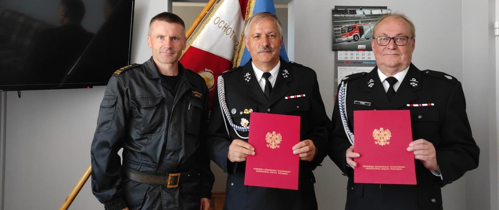 Na zdjęciu znajduje się Komendant Powiatowy ubrany w czarny mundur obok, stoją dwaj druhowie z OSP Karwia i Władysławowo. Panowie ubrani w wyjściowe mundury trzymają w rękach listy okolicznościowe.