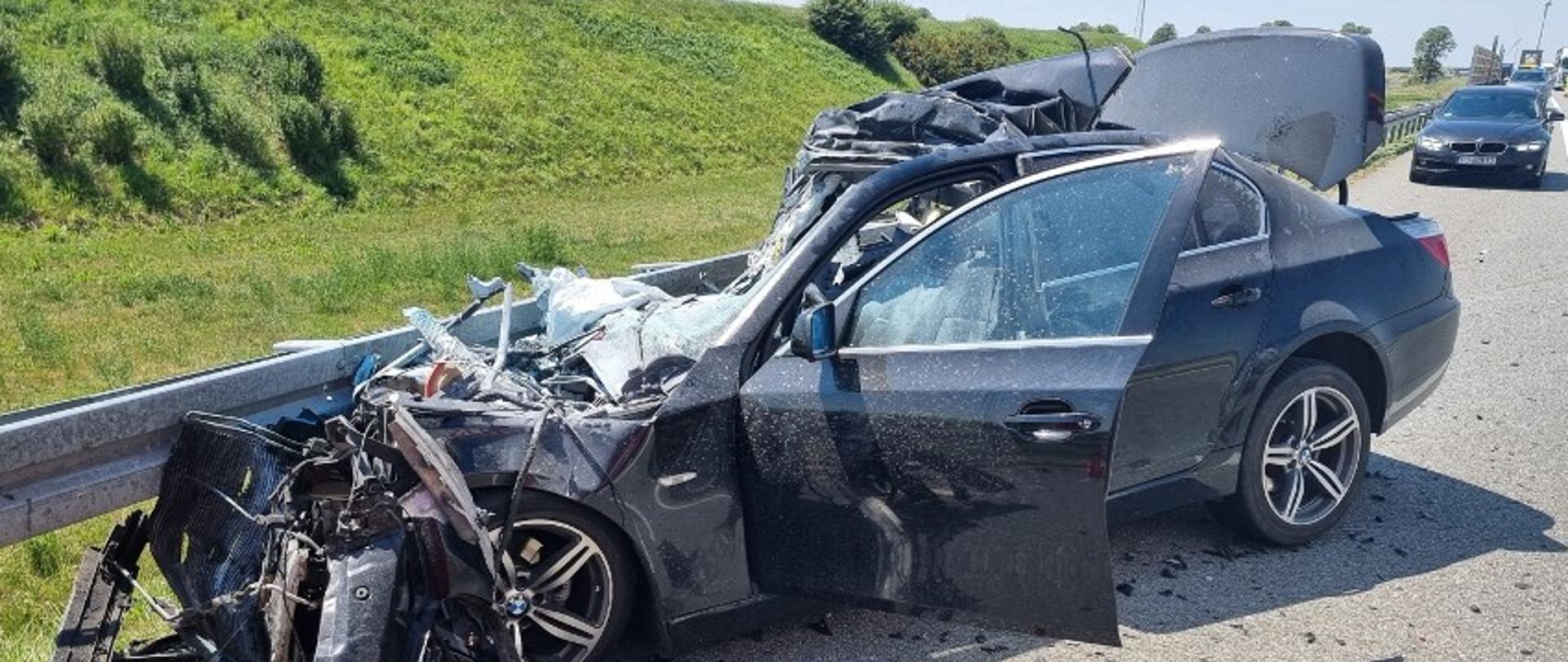 Widać mocno uszkodzony samochód od przodu, który jest przy barierkach