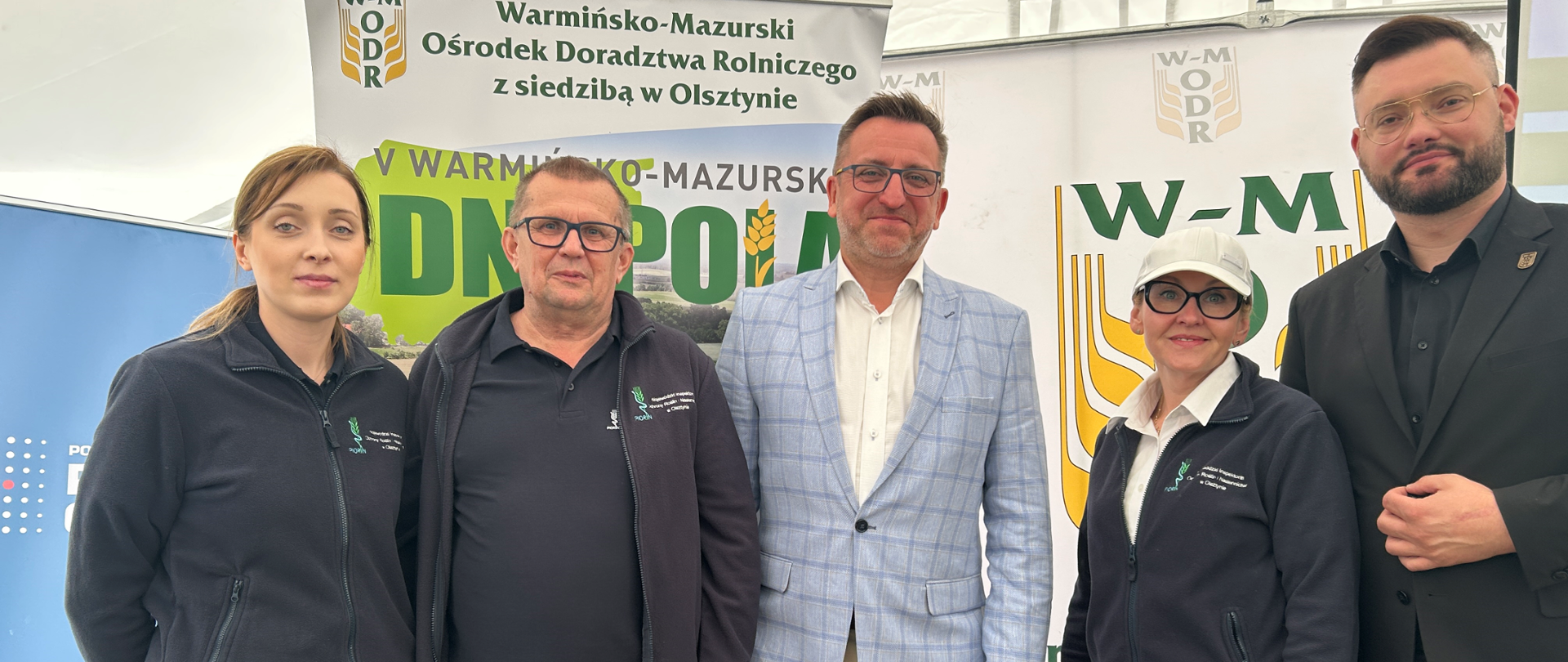 pięć osób stoi na tle banerów różnych instytucji, dwóch mężczyzn w garniturach, pozostali na ubraniach mają logo i nazwę PIORiN lub WIORiN